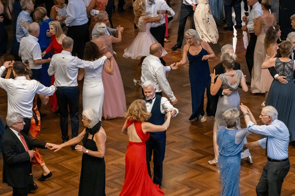 Ältere und mittelalte Paare tanzen in eleganter Abendgarderobe auf einem Holzboden bei einem festlichen Ballveranstaltung