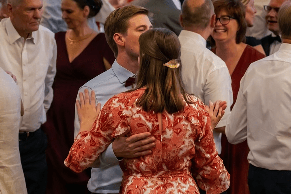 Paar tanzt eng umschlungen bei Feier im festlichen Saal mit mehreren Gästen in eleganter Kleidung