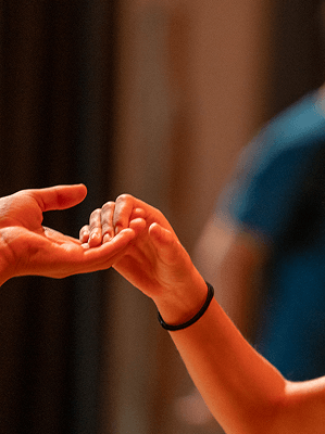 Zwei Hände greifen sich sanft in warmer Beleuchtung vor unscharfem Hintergrund