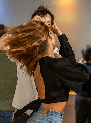 Paar tanzt eng in heller Tanzumgebung mit bewegtem Haar und schwarzem, offenem Rücken-Oberteil