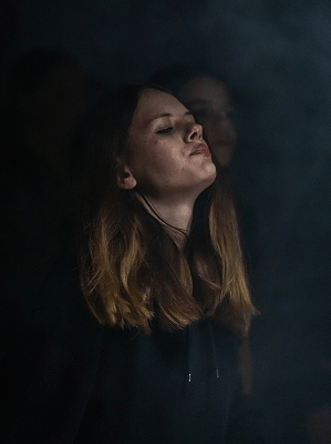 Frau mit langen braunen Haaren in dunkler Umgebung mit geschlossenen Augen und entspanntem Gesichtsausdruck