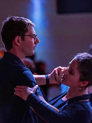 Zwei Personen tanzen eng in einem schwach beleuchteten Raum mit blauem Hintergrundlicht