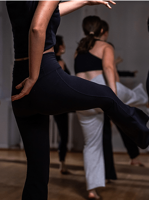 Personen in Sportkleidung beim Tanztraining in einem Studio mit Spiegelwand und Holzboden