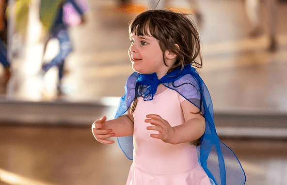 Kleines Mädchen mit rosa Kleid und blauem Tuch beim Tanzen in hellem Raum
