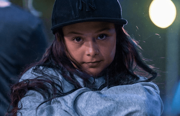 Junge Frau mit langer dunkler Haaren trägt schwarzen Baseballcap und grauen Hoodie bei Abendlicht