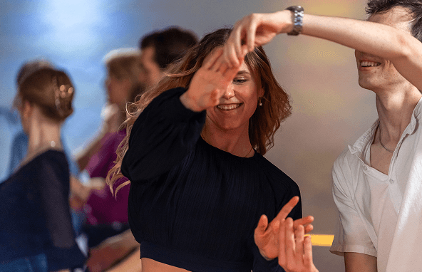 Junge Frau in schwarzem Oberteil tanzt mit lächelndem Partner auf einer Tanzveranstaltung im Innenraum