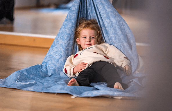 Kleines Kind mit hellbraunen Haaren liegt entspannt auf blauem Stoff in heller Innenraumumgebung