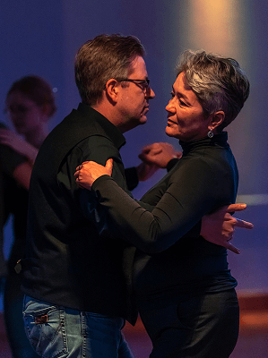 Mann und Frau tanzen eng im Tanzsaal mit gedämpftem Licht in Freizeitkleidung