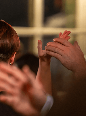 Mehrere Hände in unterschiedlichen Hauttönen klatschen im Innenraum vor einem Fenster bei gedämpftem Licht