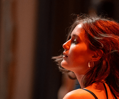 Porträt einer jungen Frau mit Locken und goldenen Creolen vor unscharfem Hintergrund bei warmem Licht