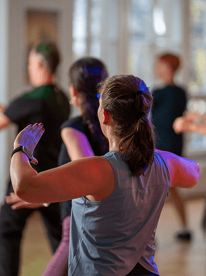 Gruppe von Personen bei einem Fitness- oder Tanzkurs in heller Trainingskleidung in einem Innenraum