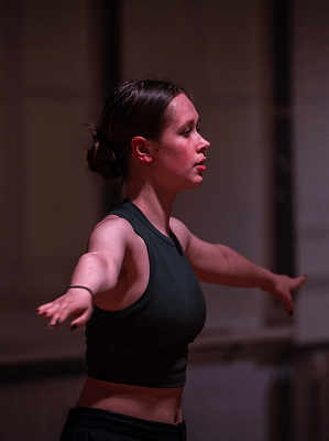 Frau in schwarzem Sporttop mit ausgestreckten Armen bei Dehnübung in Innenraum mit weicher Beleuchtung