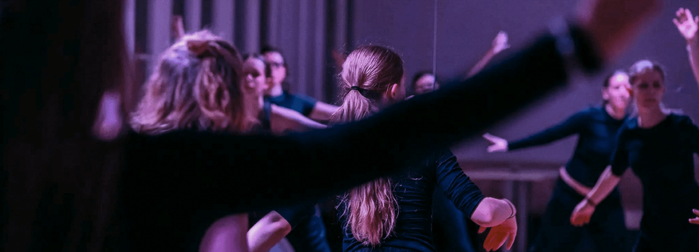 Tanzgruppe in schwarzer Kleidung bei einer Probe in einem Tanzstudio mit Spiegelwand und gedämpfter Beleuchtung