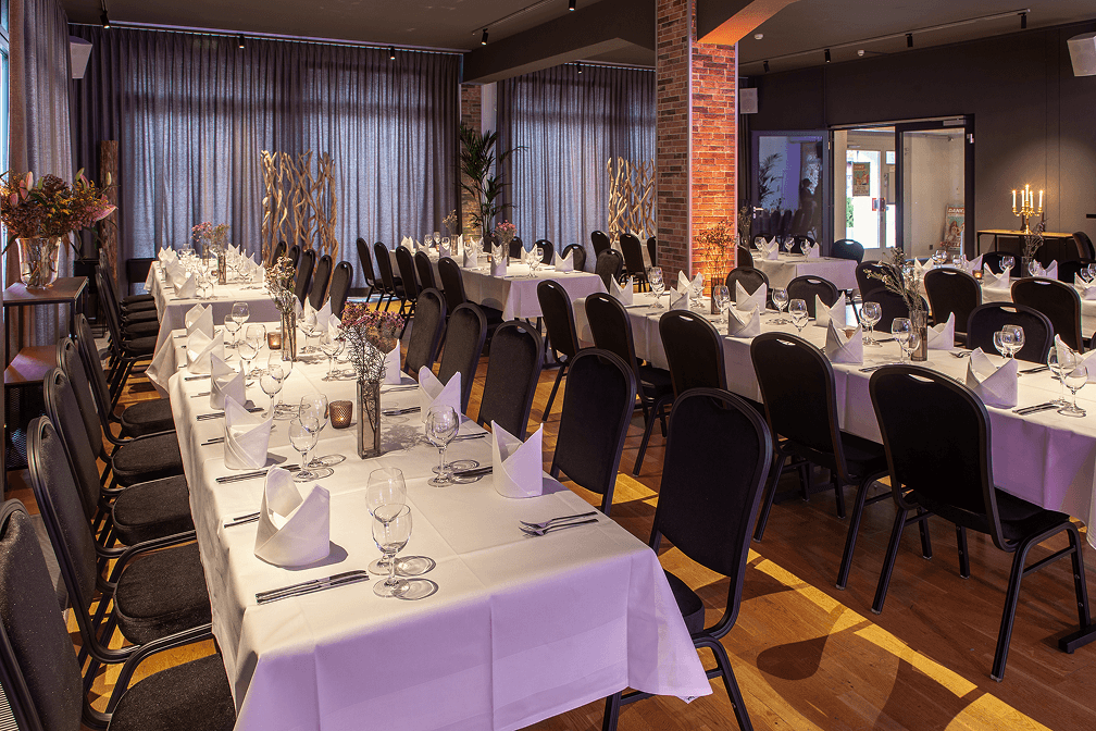 Festlich gedeckte rechteckige Tische mit weißen Tischdecken und Stoffservietten in modernem Veranstaltungsraum mit Holzfußboden