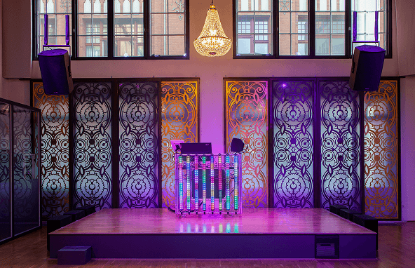 Bühne mit LED-DJ-Pult, bunten Lichtpaneelen, dekorativen Wandpaneelen und Kristallleuchter im Veranstaltungsraum