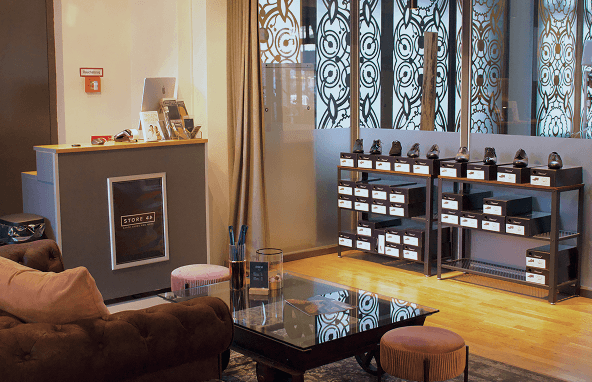 Modern eingerichteter Verkaufsraum mit Schuhregalen, gedämpfter Beleuchtung, Couch und Glastisch auf Holzboden