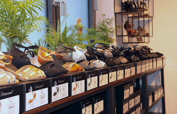 Reihe von Damenschuhen in verschiedenen Farben und Materialien auf Schuhkartons in Geschäft mit Pflanzen im Hintergrund