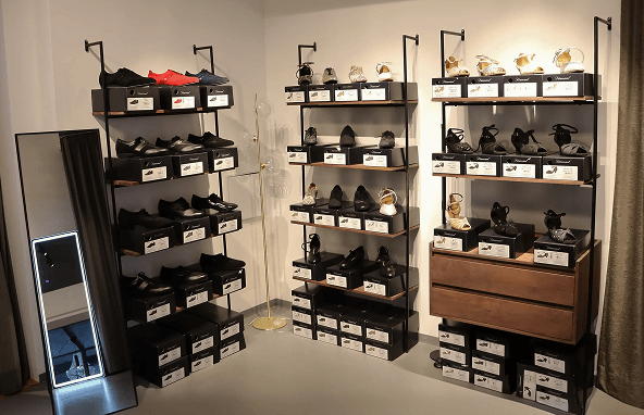 Schwarze und goldene Damenschuhe auf schwarzen Regalen neben kleinem Spiegel in modernem Raum