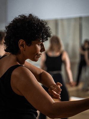 Frau mit kurzen lockigen Haaren in schwarzem Top beim Fitnesstraining in hellem Raum mit Spiegelwand