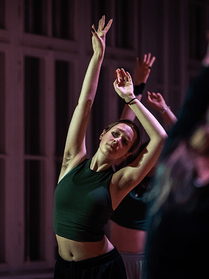 Frau in schwarzem Tanktop beim Tanz mit erhobenen Armen in einem dunklen Innenraum