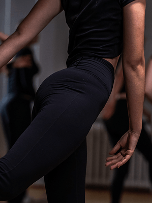 Frau in schwarzer Sportleggings und schwarzem T-Shirt beim Tanz oder Workout in Innenraum mit verschwommenem Hintergrund