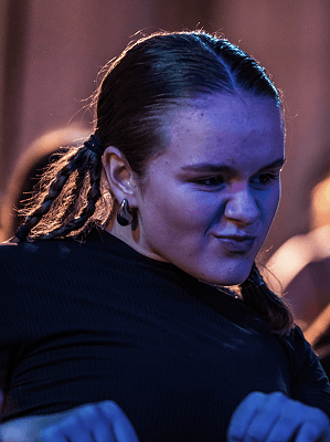 Junge Frau mit geflochtenen Zöpfen und schwarzem Oberteil bei Indoorveranstaltung mit blauem Licht