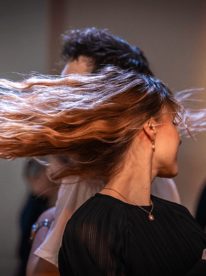 Frau mit langen braunen Haaren wirbelt kopfüber, trägt schwarzen transparenten Stoff und Goldschmuck während Tanzveranstaltung