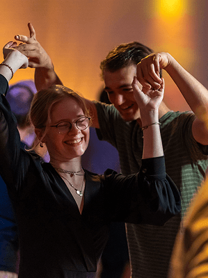 Junges Paar tanzt fröhlich in entspannter Atmosphäre mit warmem Licht im Hintergrund