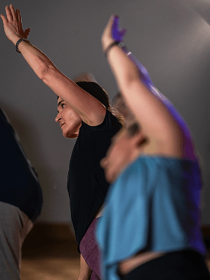 Mehrere Frauen beim Yoga mit erhobenen Armen in Innenraum mit gedämpftem Licht