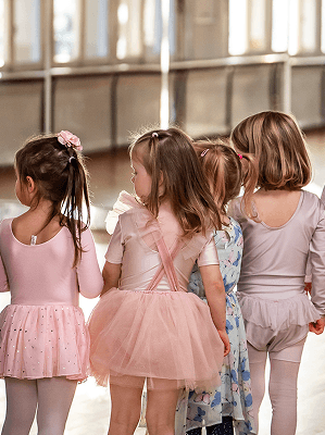 Vier Mädchen in Ballettkleidung in einem Tanzstudio mit Spiegelwand beim Ballettunterricht