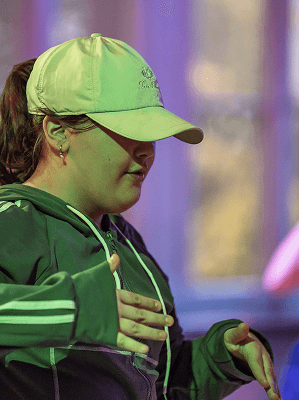 Frau mit grüner Baseballkappe und grüner Jacke in Innenraum mit unscharfem Hintergrund