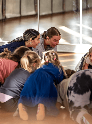 Frauen und Kinder sitzen in einem hellen Tanzstudio auf dem Holzfußboden und kommunizieren nah beieinander