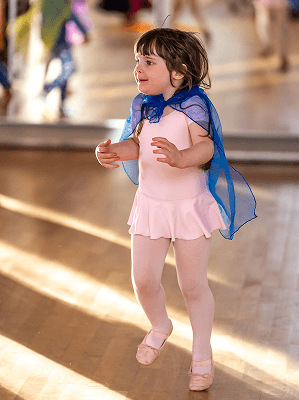 Kleines Mädchen im rosa Ballettkostüm mit blauem Umhang beim Tanzen in einem hellen Tanzstudio
