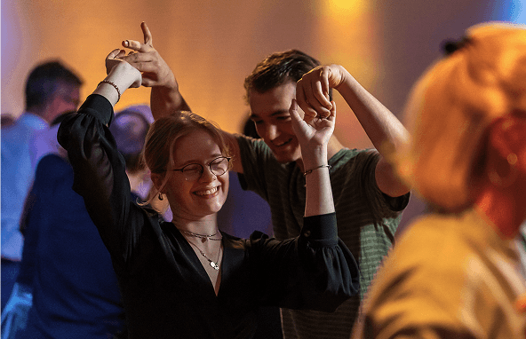 Junge Menschen tanzen fröhlich in einem warm beleuchteten Innenraum bei geselliger Veranstaltung