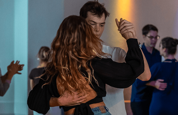 Pärchen tanzt eng in einem Raum mit anderen tanzenden Menschen im Hintergrund