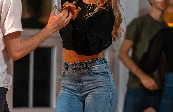 Paar beim Tanzen in Innenraum, Frau mit schwarzer Bluse und blauen Jeans, Mann in weißem T-Shirt sichtbar von der Seite