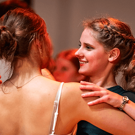 Zwei junge Frauen tanzen eng zusammen bei einem Tanzabend in warmer Beleuchtung