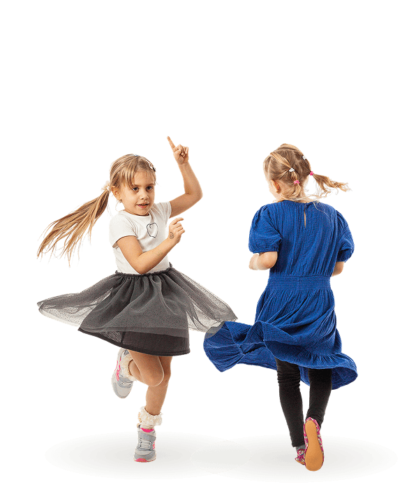 Zwei kleine Mädchen mit Zöpfen tanzen fröhlich, eines im weißen Shirt und schwarzem Rock, das andere im blauen Kleid