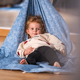 Kleines Mädchen liegt entspannt in einer Hängematte aus blau gemustertem Stoff in Innenraum