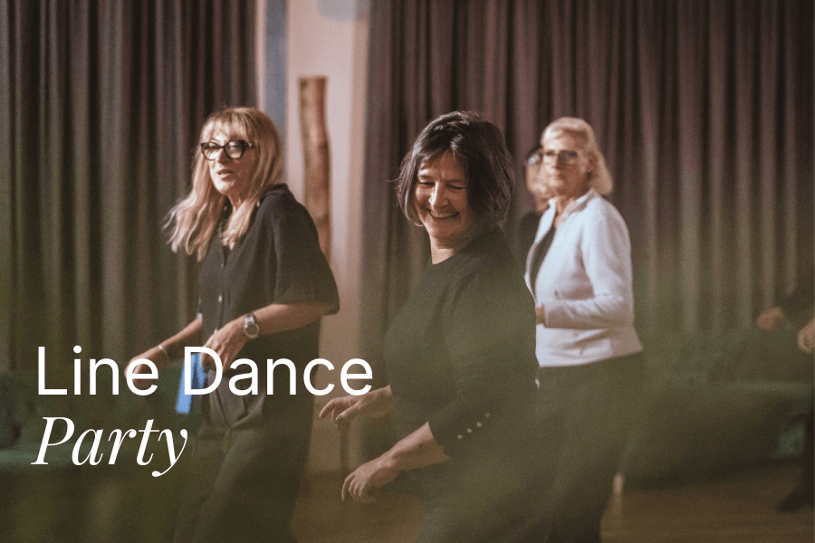 Gruppe von Erwachsenen beim Line Dance in einem Saal mit Vorhängen und gedimmtem Licht