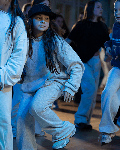 Gruppe junger Menschen in Freizeitkleidung beim Tanzen in Innenraum mit Holzboden und gedämpfter Beleuchtung