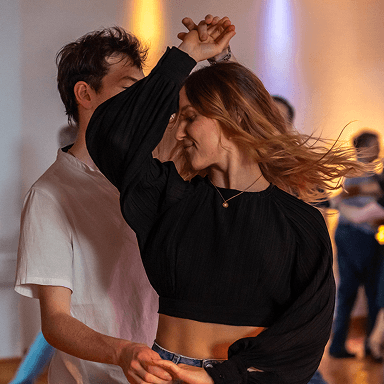 Paar tanzt in einem Raum mit warmem Licht die Frau trägt schwarzen langen Puffärmeln und blauen Jeans