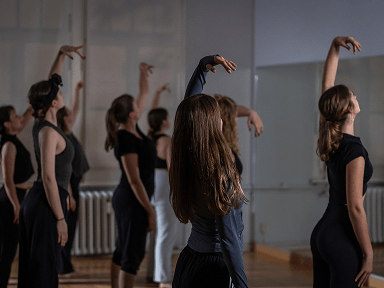 Mehrere Frauen in Sportkleidung beim Balletttraining in einem Tanzstudio mit Spiegelwand und Holzboden