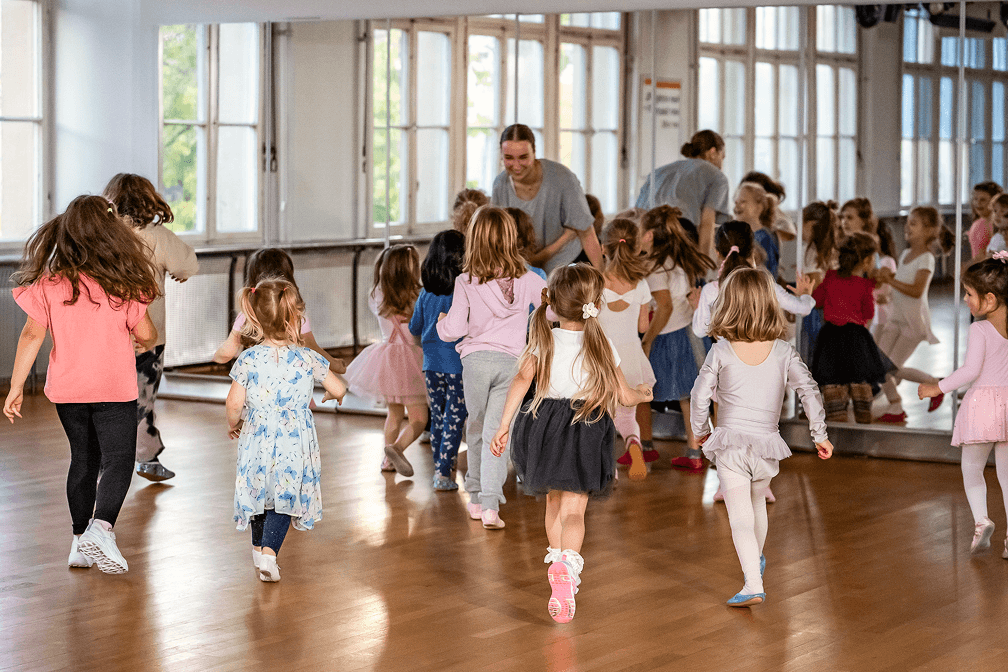 Kinder laufen lachend durch den Tanzsaal auf eine Tanzlehrerin zu, die sie beim Kindertanz anleitet