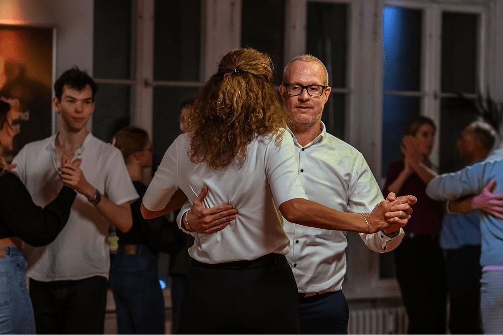 Paar tanzt im Vordergrund im Tanzsaal, im Hintergrund weitere Paare während eines Paartanzkurses