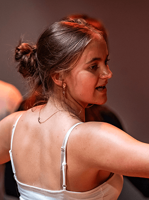 Junge Frau mit hochgesteckten braunen Haaren trägt weißen Träger-Top und goldene Ohrringe in Innenraum