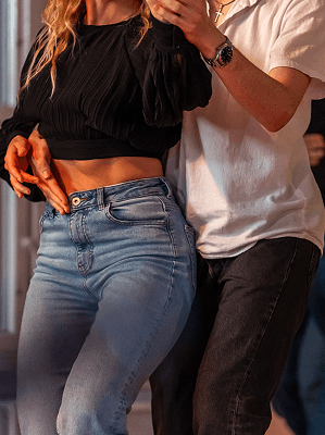 Paar beim Tanzen in Freizeitkleidung, Frau mit schwarzem Oberteil und blauer Jeans, Mann mit weißem T-Shirt und schwarzer Hose