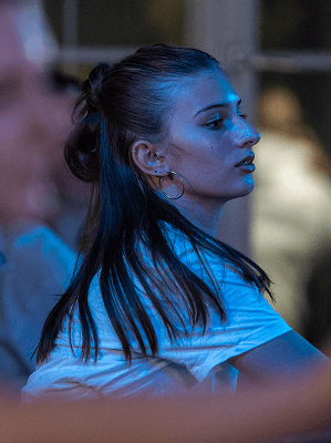 Junge Frau mit Zopf und weißen T-Shirt bei Tanzveranstaltung mit blauem Bühnenlicht