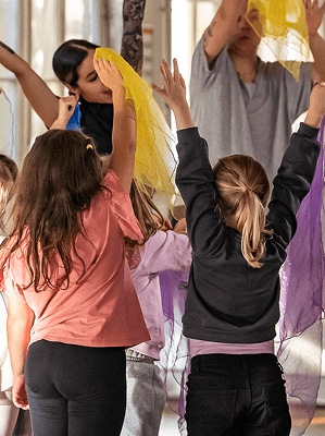 Kinder tanzen und bewegen sich mit bunten Tüchern in einem hellen Innenraum bei einer Tanzstunde