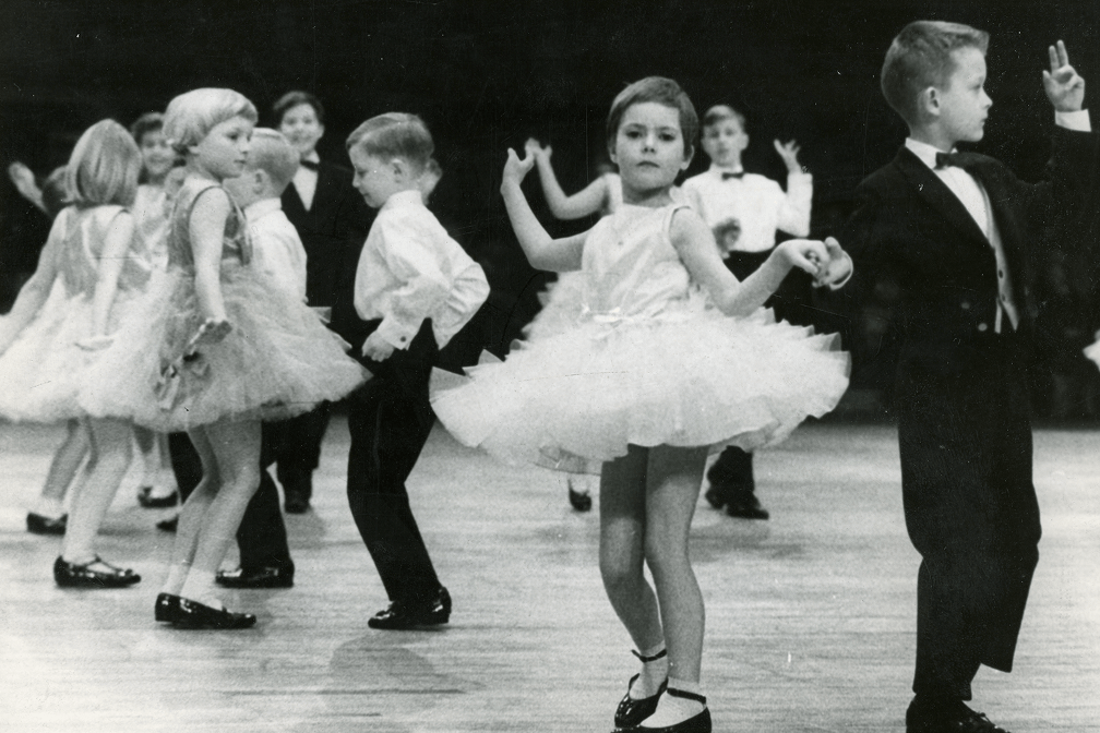 Schwarzweißfoto von Kindern im Ballettkleid und Anzug beim Paartanz auf Holzfußboden in Saal